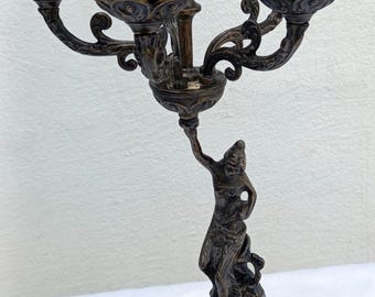 May include: A five-arm bronze candelabra with a decorative base and a sculpted figure of a woman holding a torch. The candelabra has a dark brown patina and intricate details.