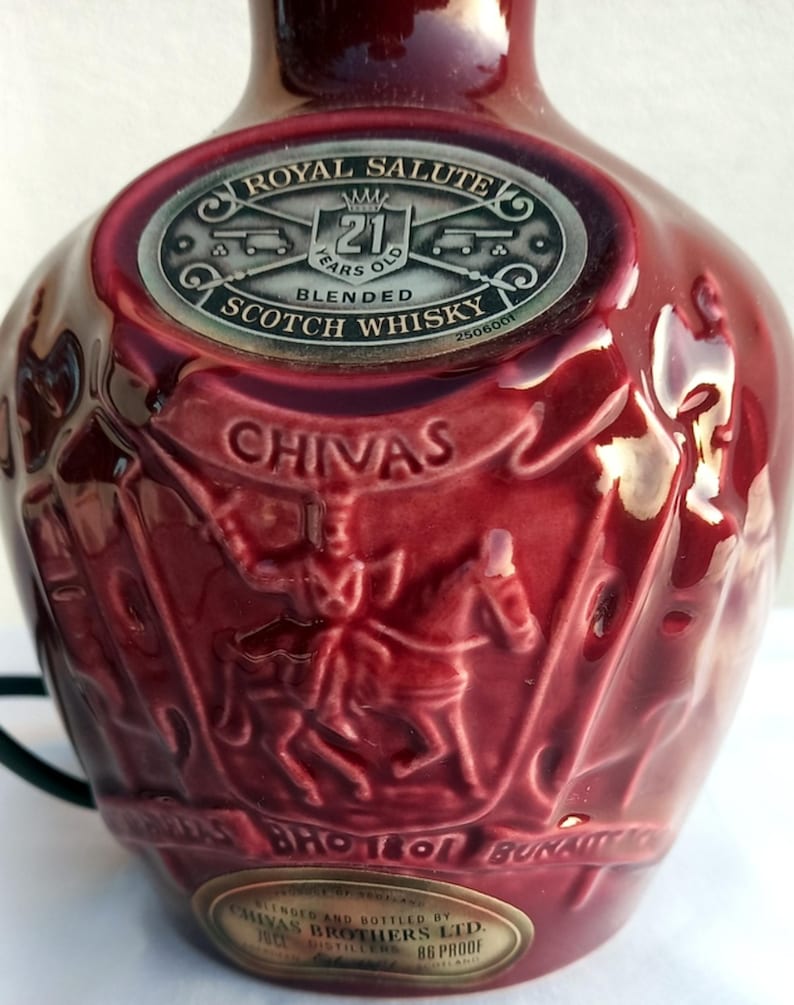 Może przedstawiać: Bordowa ceramiczna butelka 21-letniej mieszanej szkockiej whisky Royal Salute. Butelka posiada wytłoczone detale jeźdźc&oacute;w oraz napisy "Chivas" i "Royal Salute". Srebrna etykieta wskazuje wiek whisky.