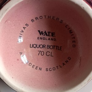 Może przedstawiać: Zbliżenie dna butelki po alkoholu Wade England. Butelka jest w kolorze jasnor&oacute;żowym i ma czarny napis "Chivas Brothers Limited" oraz "Liquor Bottle 70 CL". Widoczny jest r&oacute;wnież napis "Aberdeen Scotland".