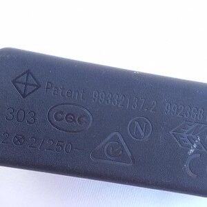 Może przedstawiać: Czarny, prostokątny element elektryczny z r&oacute;żnymi oznaczeniami i tekstem. Tekst zawiera "Patent 99332137.2 99238813.9", "303", "2 &Oslash; 2/250-" oraz kilka symboli, w tym romb i tr&oacute;jkąt.