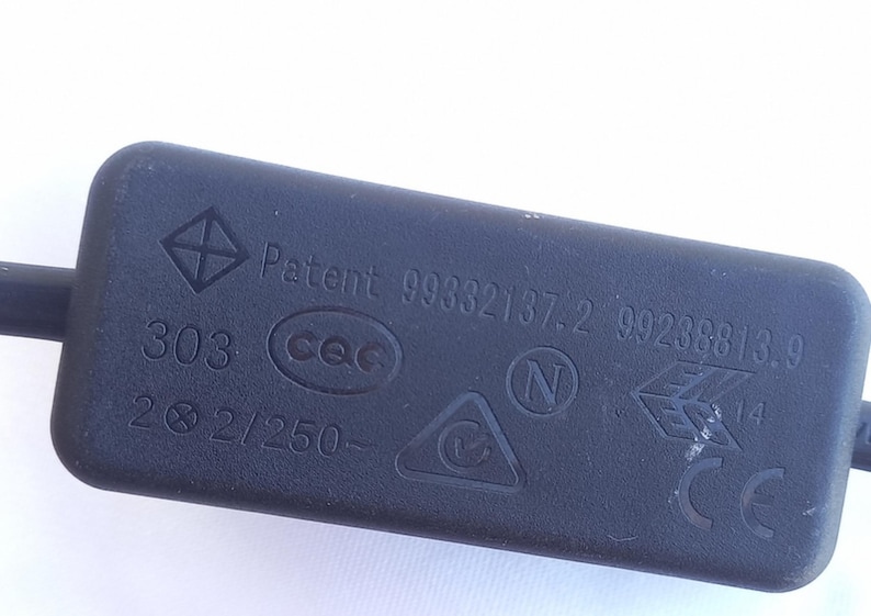 Może przedstawiać: Czarny, prostokątny element elektryczny z r&oacute;żnymi oznaczeniami i tekstem. Tekst zawiera "Patent 99332137.2 99238813.9", "303", "2 &Oslash; 2/250-" oraz kilka symboli, w tym romb i tr&oacute;jkąt.
