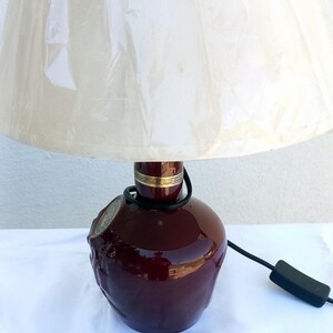 Może przedstawiać: Bordowa ceramiczna lampa stołowa z kremowym abażurem. Podstawa lampy ma teksturowany wz&oacute;r i złoty pasek u g&oacute;ry. Widoczny czarny przew&oacute;d i włącznik/wyłącznik.