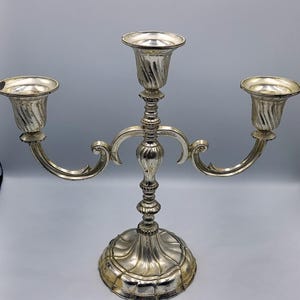 Può includere: Candelabro in argento a tre bracci con una base decorativa e dettagli decorativi.