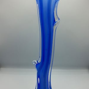 May include: A tall, slender glass vase featuring a vibrant blue core encased in clear glass. The vase has a flared, ruffled rim and a wide, multi-lobed base. The body of the vase displays organic, flowing vertical lines and subtle protrusions.