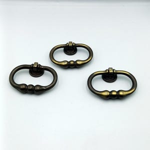 May include: Three antique brass oval cabinet door pulls with a rounded design.