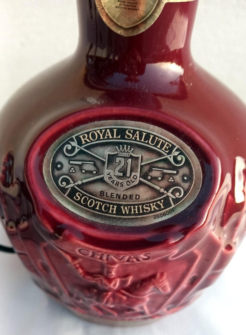 Może przedstawiać: Bordowa butelka Royal Salute 21 Years Old Blended Scotch Whisky. Etykieta zawiera napisy "Royal Salute" i "21 Years Old Blended Scotch Whisky". Butelka ma teksturowaną powierzchnię i dekoracyjny wz&oacute;r.