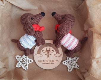 Op de afbeelding: Twee bruine gehaakte teckelhondjes met rood-wit gestreepte shirts. De knuffels zitten in een bruine papieren cadeaudoos met een houten cirkel waarop "Giraffeletoys your rainbow choice" staat.
