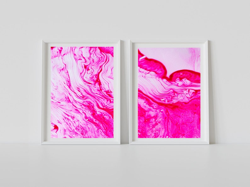 K&ouml;nnte beinhalten: Zwei gerahmte abstrakte Kunstdrucke mit wirbelnden Mustern in Pink und Wei&szlig;. Die Drucke sind in wei&szlig;en Rahmen und h&auml;ngen an einer wei&szlig;en Wand.