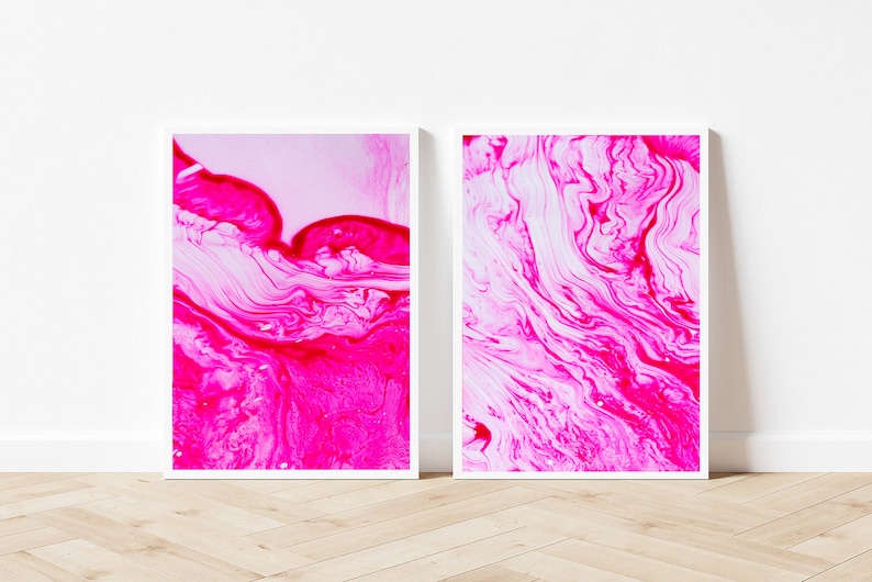K&ouml;nnte beinhalten: Zwei gerahmte abstrakte Kunstdrucke mit wirbelnden Mustern in Pink und Wei&szlig;. Die Drucke sind in wei&szlig;en Rahmen und h&auml;ngen an einer wei&szlig;en Wand.