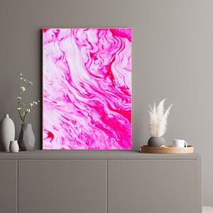K&ouml;nnte beinhalten: Abstrakter Kunstdruck mit wirbelnden Mustern in Pink und Wei&szlig;. Der Druck ist gerahmt und h&auml;ngt an einer grauen Wand &uuml;ber einem grauen Schrank.