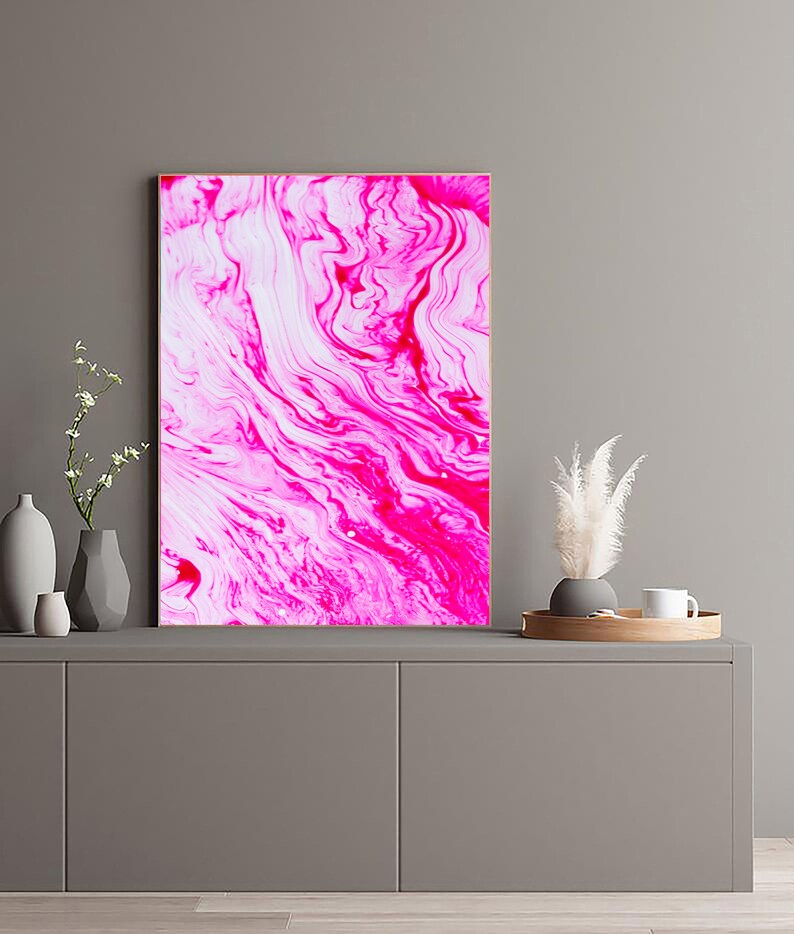 K&ouml;nnte beinhalten: Abstrakter Kunstdruck mit wirbelnden Mustern in Pink und Wei&szlig;. Der Druck ist gerahmt und h&auml;ngt an einer grauen Wand &uuml;ber einem grauen Schrank.