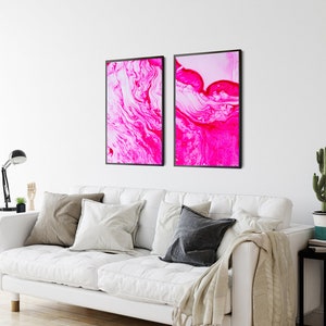 K&ouml;nnte beinhalten: Zwei gerahmte abstrakte Kunstdrucke mit wirbelnden Mustern in Pink und Wei&szlig;. Die Drucke sind in schwarzen Rahmen und h&auml;ngen an einer wei&szlig;en Wand.