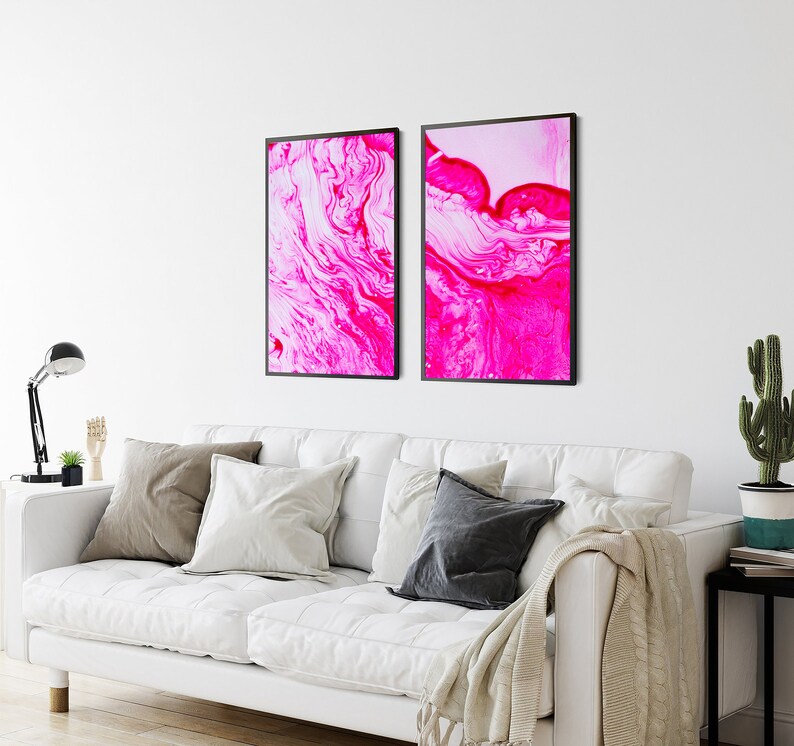 K&ouml;nnte beinhalten: Zwei gerahmte abstrakte Kunstdrucke mit wirbelnden Mustern in Pink und Wei&szlig;. Die Drucke sind in schwarzen Rahmen und h&auml;ngen an einer wei&szlig;en Wand.