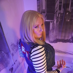 May include: A blonde wig, denim vest with a red "R" patch, and black and white striped sleeves. The outfit is completed with a denim skirt and black leggings. The image includes the text "Queen Riot".