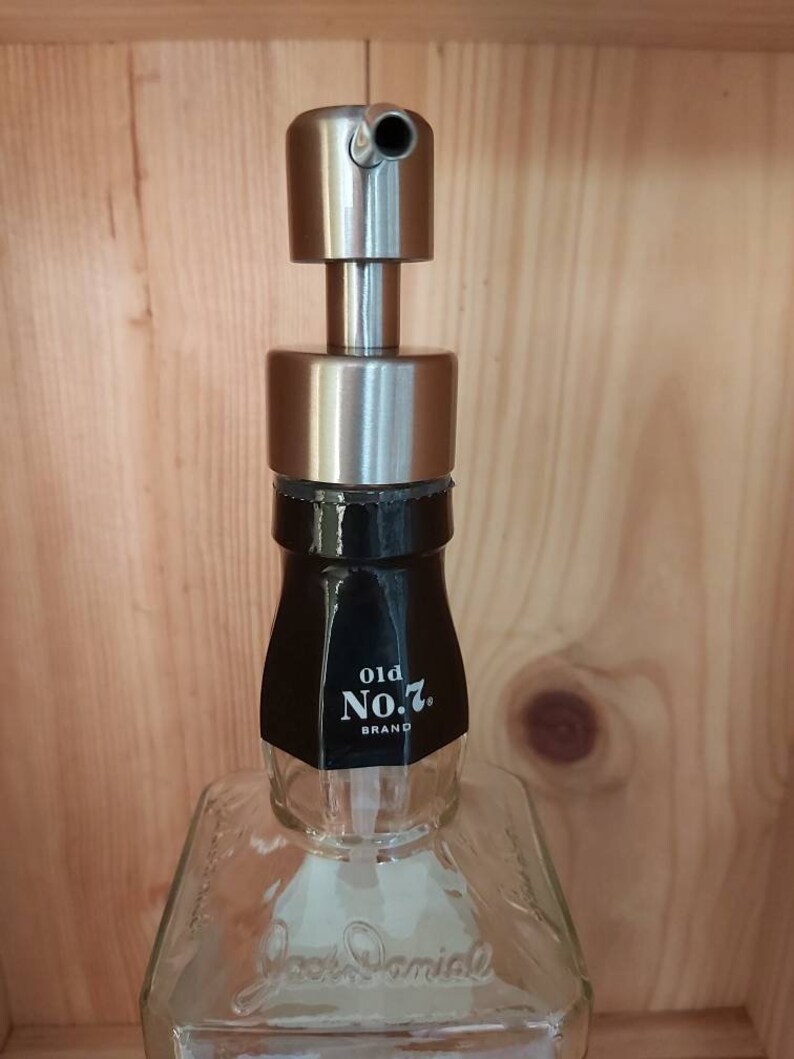 May include: A clear glass bottle with a black label that reads "old No. 7. BRAND" and a silver soap dispenser pump on top. The bottle is sitting on a wooden surface.