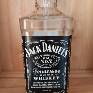 May include: A clear glass bottle with a black label that reads "Jack Daniel's Old No.7 Brand Tennessee Sour Mash Whiskey". The label also includes the text "Distilled and Bottled by Jack Daniel Distillery Lynchburg, Tennessee 37352 U.S.A. 70cl 40% Vol."