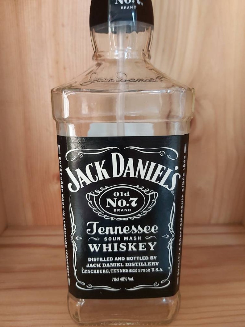 May include: A clear glass bottle with a black label that reads "Jack Daniel's Old No.7 Brand Tennessee Sour Mash Whiskey". The label also includes the text "Distilled and Bottled by Jack Daniel Distillery Lynchburg, Tennessee 37352 U.S.A. 70cl 40% Vol."