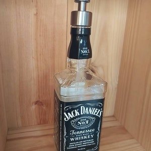 May include: A clear glass bottle with a black label that reads "Jack Daniel's Old No.7 Brand Tennessee Sour Mash Whiskey". The bottle has a silver pump dispenser on top.