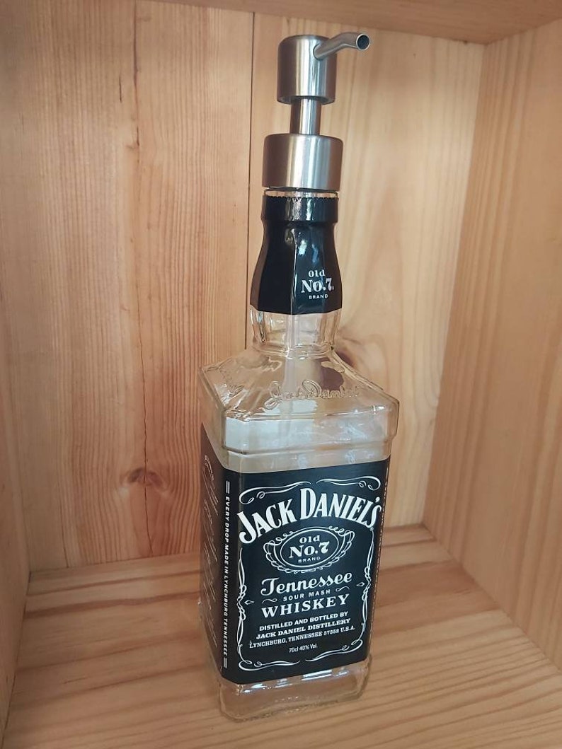 May include: A clear glass bottle with a black label that reads "Jack Daniel's Old No.7 Brand Tennessee Sour Mash Whiskey". The bottle has a silver pump dispenser on top.