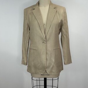 K&ouml;nnte beinhalten: Ein beigefarbener Blazer mit einem Ein-Knopf-Verschluss und zwei Vordertaschen. Der Blazer wird auf einer Schaufensterpuppe pr&auml;sentiert. Auf dem Etikett der Schaufensterpuppe steht "Made in China".