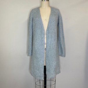 May include: A light blue cardigan with a sparkly texture. The cardigan is open at the front and has long sleeves.
