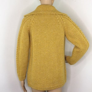 May include: A yellow knitted cardigan with a high collar and long sleeves.
