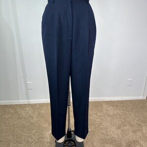May include: Navy blue high-waisted trousers with a button closure and pleats. The pants are displayed on a mannequin. The trousers have a straight leg design and are made of a solid, dark blue fabric.