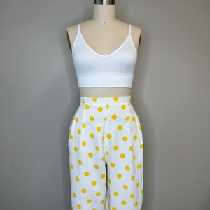May include: White crop top with a v-neck and yellow polka dot pants.