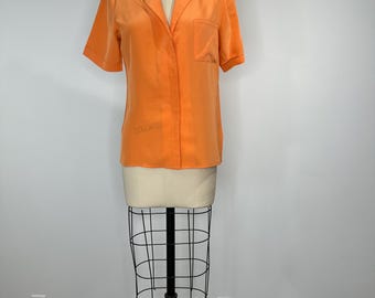 Puede incluir: Camisa naranja de manga corta con bolsillo en el pecho, exhibida en un maniquí. La palabra "COLLARS" es visible en la camisa. La camisa tiene un cuello clásico y un corte relajado.