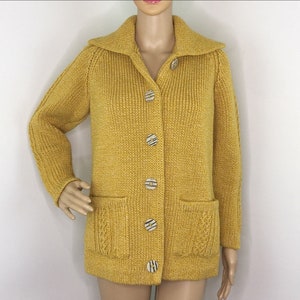 May include: A mustard yellow knitted cardigan with a collared neckline and six large, round buttons. The cardigan has two patch pockets on the front.