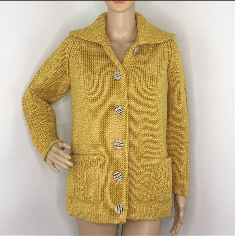 May include: A mustard yellow knitted cardigan with a collared neckline and six large, round buttons. The cardigan has two patch pockets on the front.