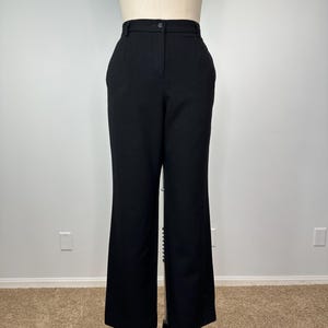 May include: Black high-waisted trousers with a button closure and side pockets. The pants have a wide-leg design and are displayed on a mannequin. The trousers are made of a solid black fabric.