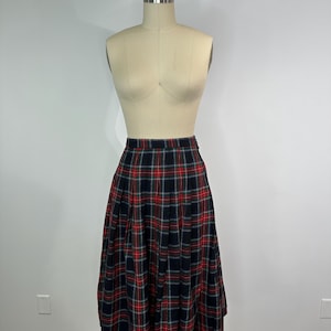 May include: A vintage pleated skirt with a tartan pattern. The skirt is predominantly black, with red and green checks. It is displayed on a mannequin. The skirt's design is a classic style.
