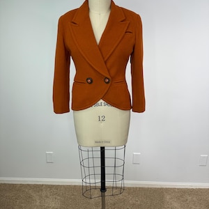 May include: A burnt orange blazer with a double-breasted design, displayed on a mannequin. The blazer features two dark brown buttons and a classic lapel. The mannequin is size 12.