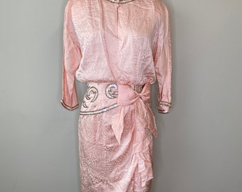 May include: A light pink vintage dress with a unique pattern and long sleeves. The dress features a beaded neckline and waist detail, with a draped skirt and a bow at the waist. The dress is displayed on a mannequin.