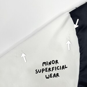 May include: Close-up of a white fabric with black trim. The text "MINOR SUPERFICIAL WEAR" is written in black. The image shows minor wear and tear on the fabric.