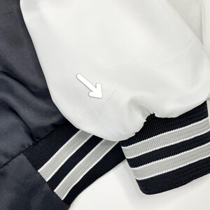 May include: Close-up of two satin bomber jacket sleeves. One sleeve is black, the other is white. Both have black cuffs with gray and white stripes. The jackets are likely part of a set or a matching style.