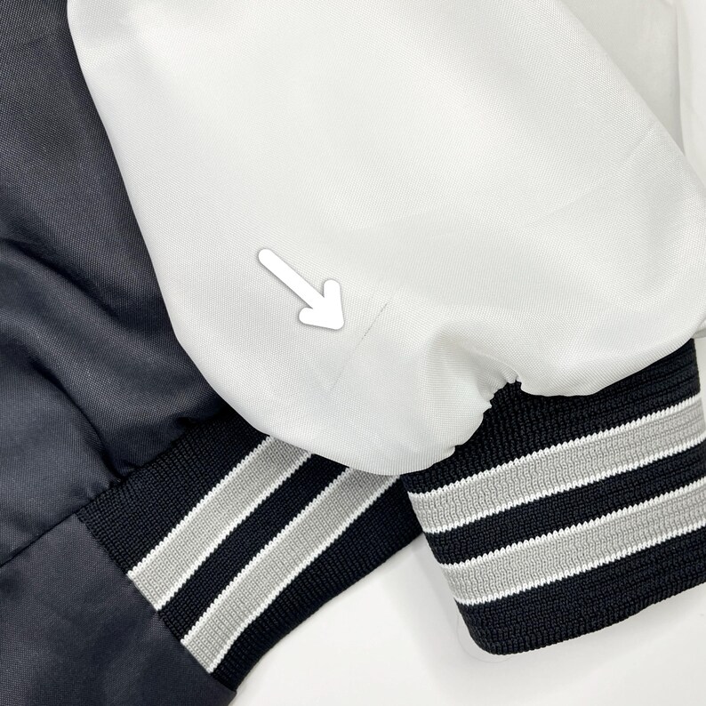 May include: Close-up of two satin bomber jacket sleeves. One sleeve is black, the other is white. Both have black cuffs with gray and white stripes. The jackets are likely part of a set or a matching style.