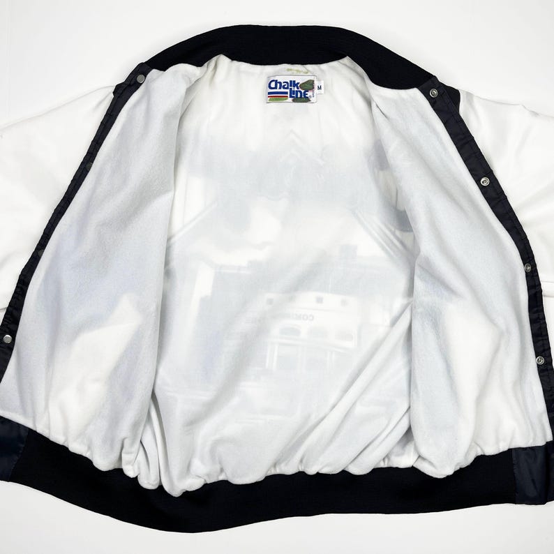 May include: White and black vintage jacket with a snap front closure. The jacket has a black collar and trim, and a printed interior lining. The Chalk Line brand label is visible at the neck. The jacket is open, showing the interior lining.