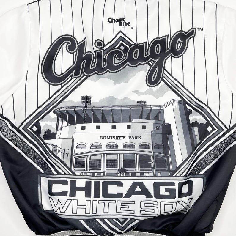 May include: White and black Chicago White Sox satin jacket with pinstripes. Features the word "Chicago" in a cursive font, a diamond-shaped graphic of Comiskey Park, and the words "Chicago White Sox". The jacket is from Chalk Line.