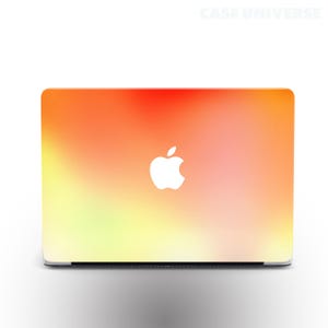 Pode incluir: Um computador portátil com um design degradê colorido na tampa. O design passa do amarelo para o laranja para o vermelho. O logotipo da Apple está em branco no centro da tampa.
