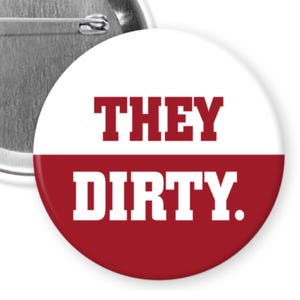 May include: A round button with a white top half and a red bottom half. The text "THEY" is in red block letters above "DIRTY." in red block letters. The back of the button is silver.