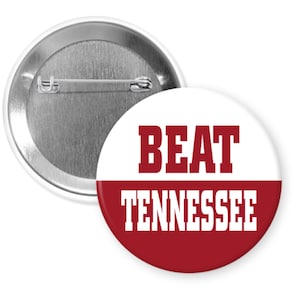 May include: A white and red button with the text "BEAT TENNESSEE" in bold white letters on a red background. The top half of the button is white with the text "BEAT" in bold red letters.