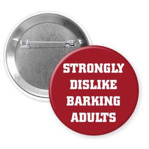 May include: A red button with the text "STRONGLY DISLIKE BARKING ADULTS" in white, with a silver pin back. The button is round and has a shiny finish. The text is in a bold, sans-serif font.