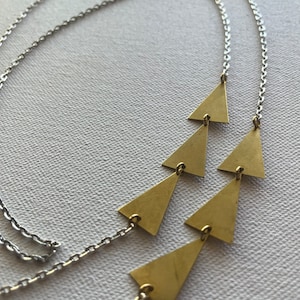 May include: A silver chain necklace with a layered pendant of five gold triangles.