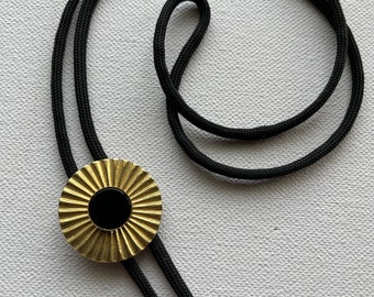 May include: A black bolo tie with a gold sunburst pendant featuring a black onyx center.