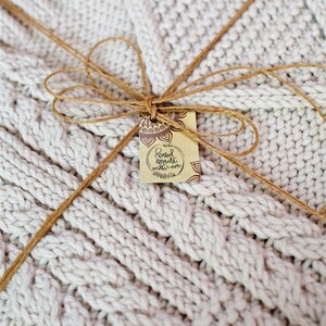 Puede incluir: Una manta de punto blanco atada con un lazo de cuerda marr&oacute;n y una etiqueta que dice "Hand made with love".