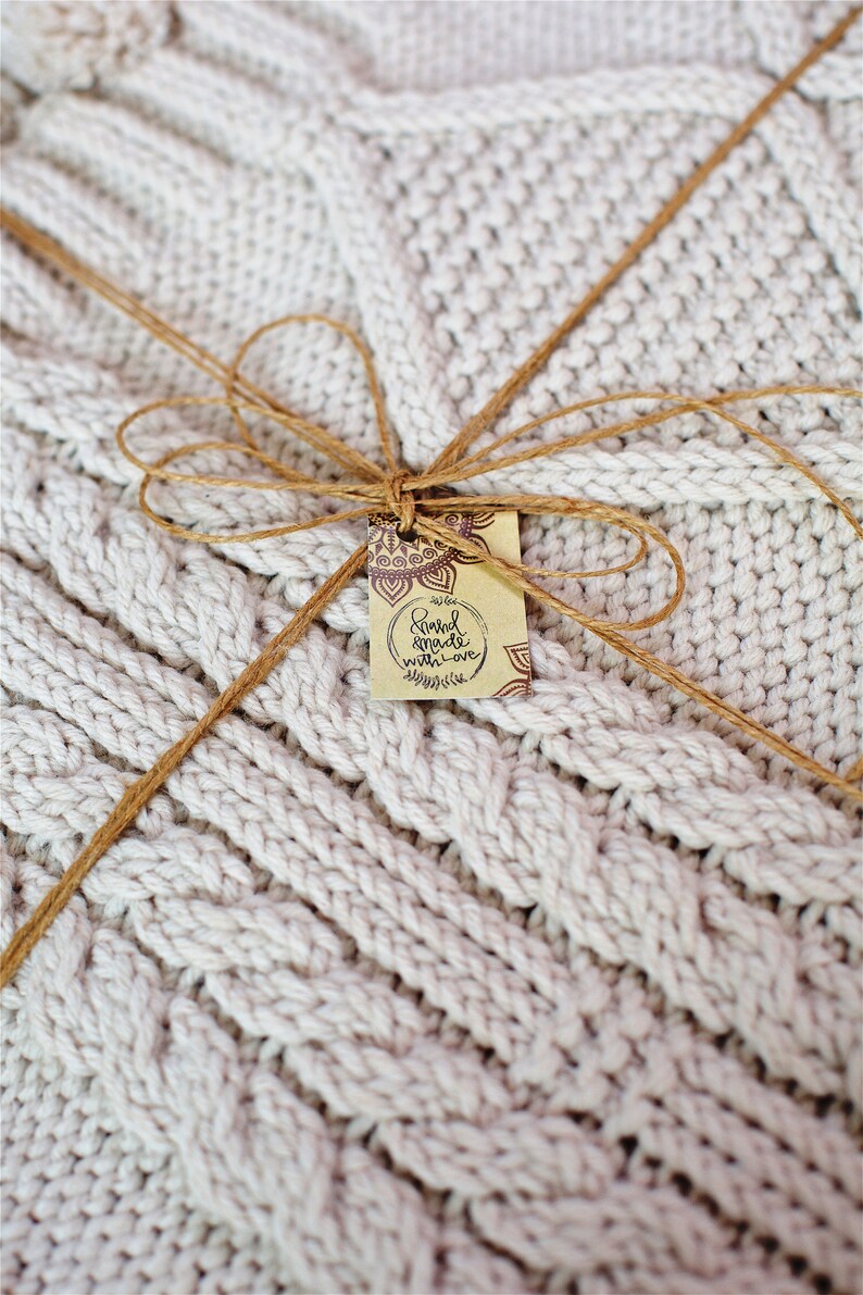 Puede incluir: Una manta de punto blanco atada con un lazo de cuerda marr&oacute;n y una etiqueta que dice "Hand made with love".