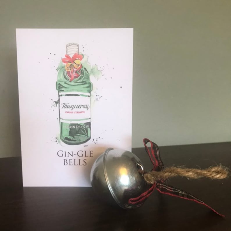 Puede incluir: Una tarjeta de felicitaci&oacute;n con una ilustraci&oacute;n en acuarela de una botella de ginebra Tanqueray, con las palabras "GIN-GLE BELLS" debajo. Una campana plateada con una cinta escocesa roja y negra y cuerda est&aacute; al lado de la tarjeta.