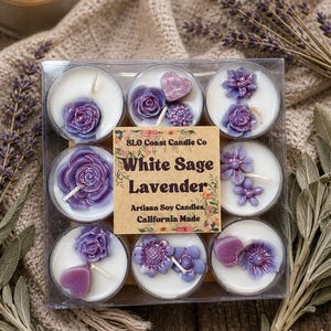 Op de afbeelding: Een doos met negen witte sojawas kaarsen, elk met paarse bloemen en hart decoraties. De transparante doos heeft een label met de tekst "White Sage Lavender" en "Artisan Soy Candles, California Made." De kaarsen worden gepresenteerd met gedroogde lavendel.